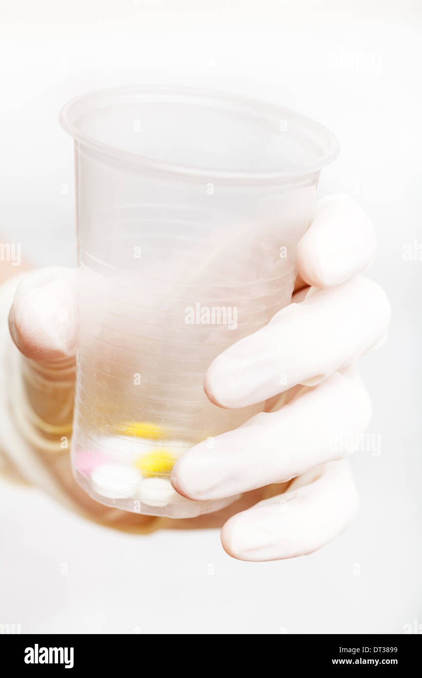 behandschuhten Hand hält Plastikbecher mit Pillen auf weißem Hintergrund Stockfoto