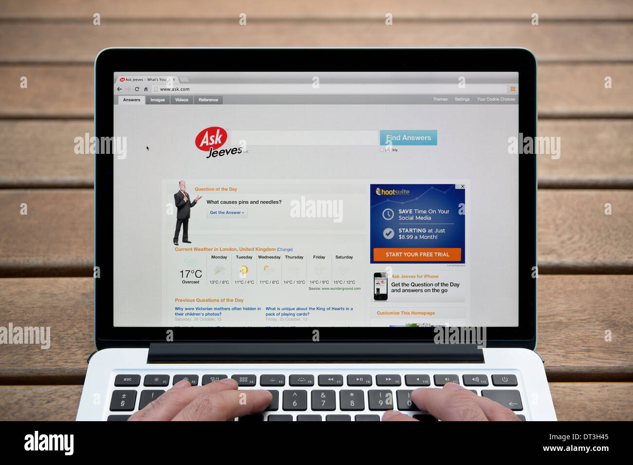 Die Ask Jeeves-Website auf einem MacBook Hintergrund eine Holzbank im Freien einschließlich eines Mannes Finger (nur zur redaktionellen Verwendung). Stockfoto