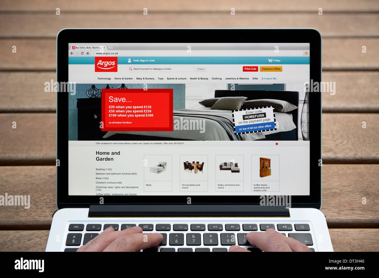 Die Argos-Website auf einem MacBook Hintergrund eine Holzbank im Freien einschließlich eines Mannes Finger (nur zur redaktionellen Verwendung). Stockfoto