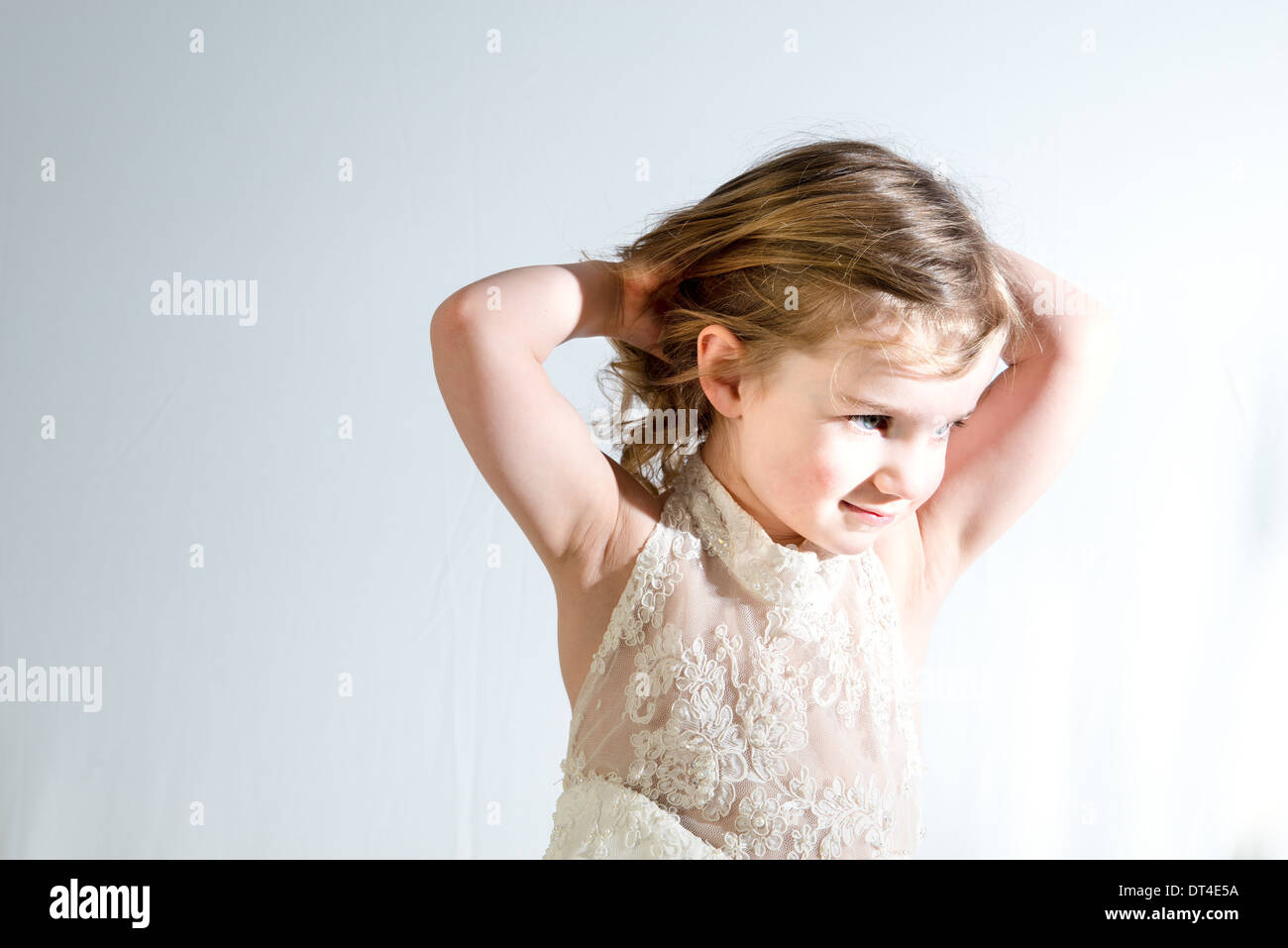 Ein junges Mädchen trägt ein Erwachsener Hochzeitskleid und Weg von der Kamera aber mit ihr lächelnd die Hände in ihr Haar. Stockfoto