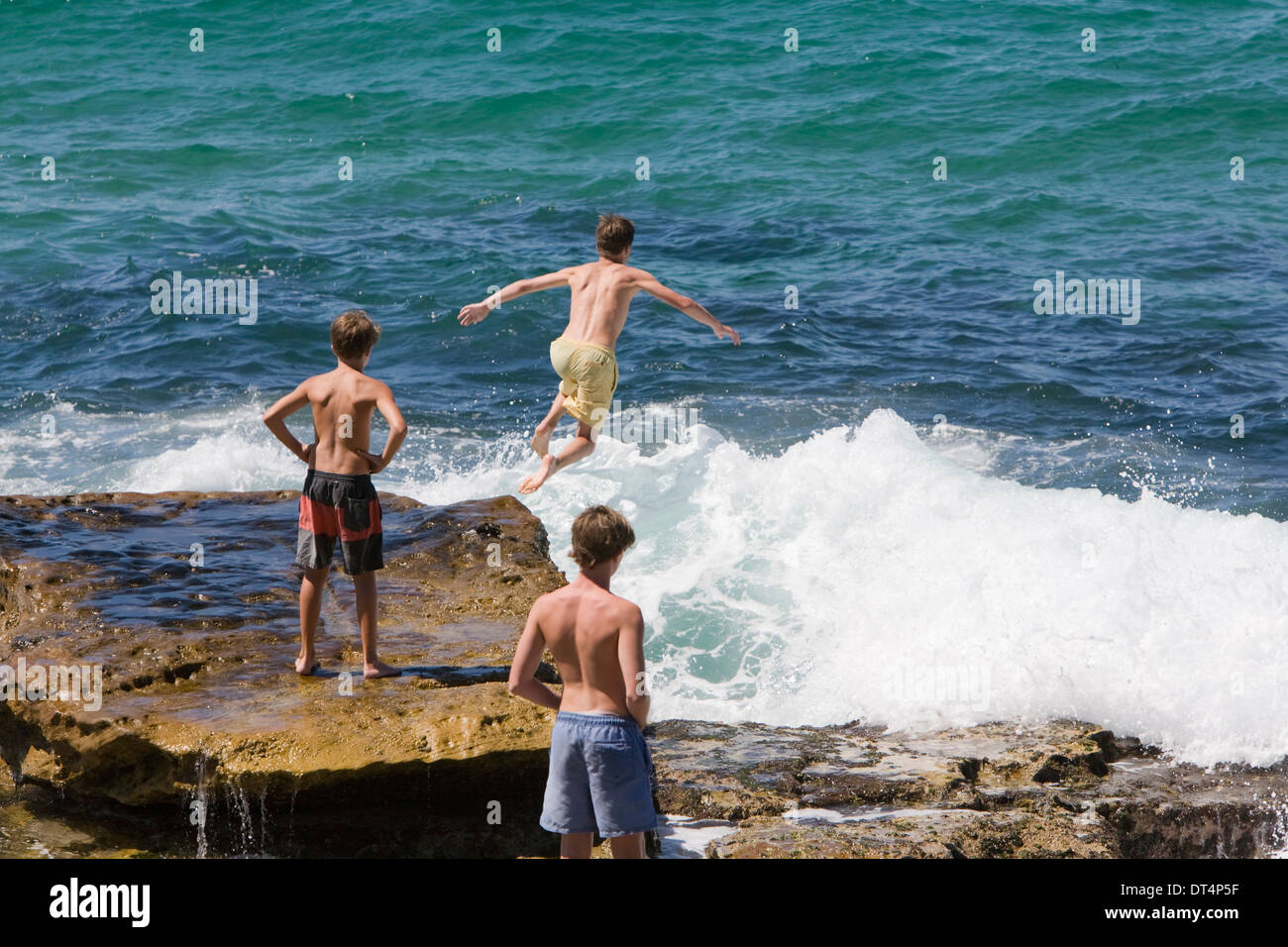 drei junge Burschen, die ein Spiel springen deaktiviert die Felsen in der Nähe von Manly Beach, Sydney, Australien Stockfoto