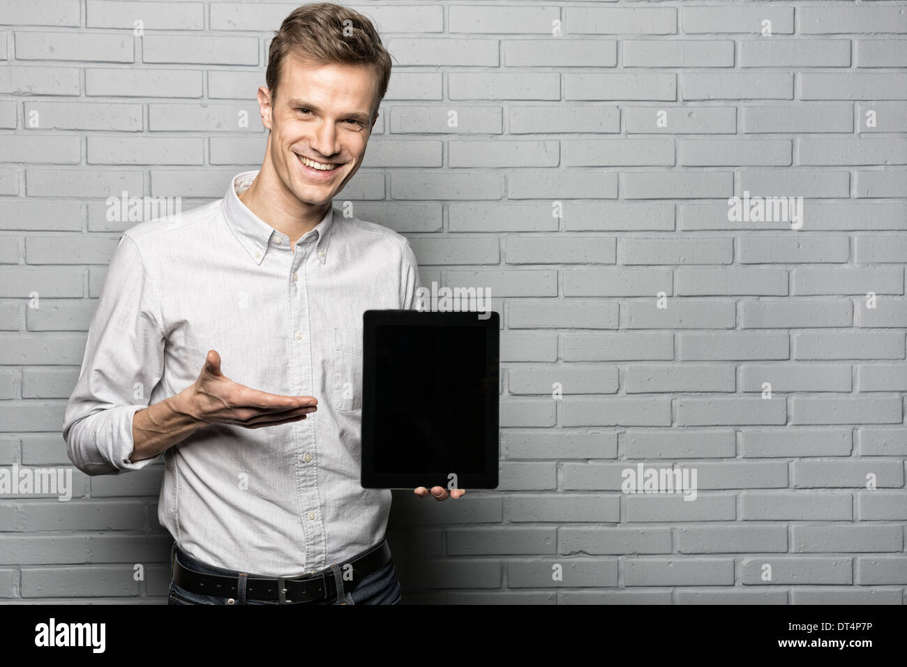 Portrait von männlichen Model präsentiert Tablet auf Studio mit grauem Hintergrund, auf der Suche nach Kamera Stockfoto