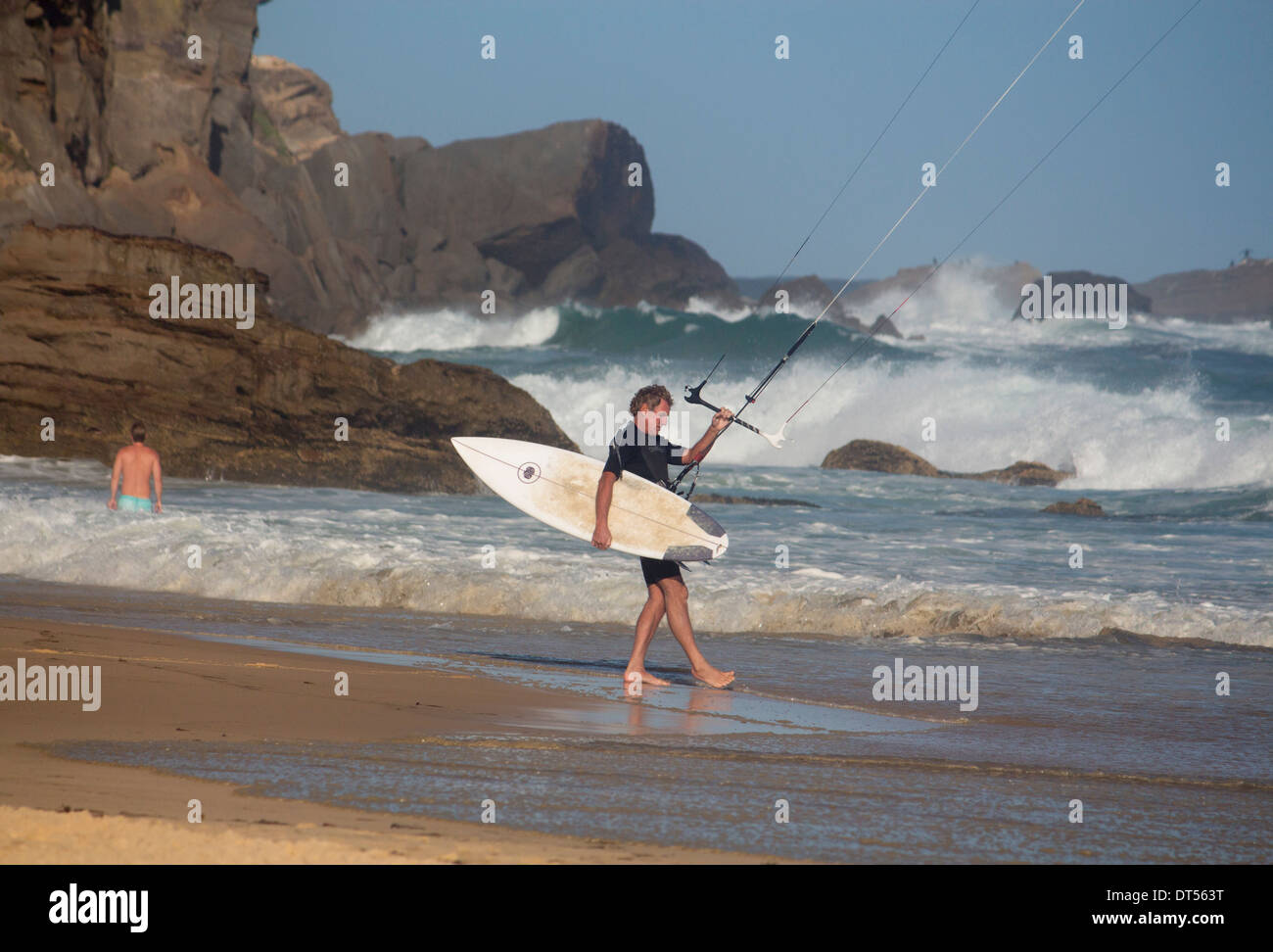 Kite Surfen Kitesurfer zu Fuß ins Meer mit Surfbrett und Kite Felsen und Klippen hinter Rothaarige Beach New South Wales Australien Stockfoto