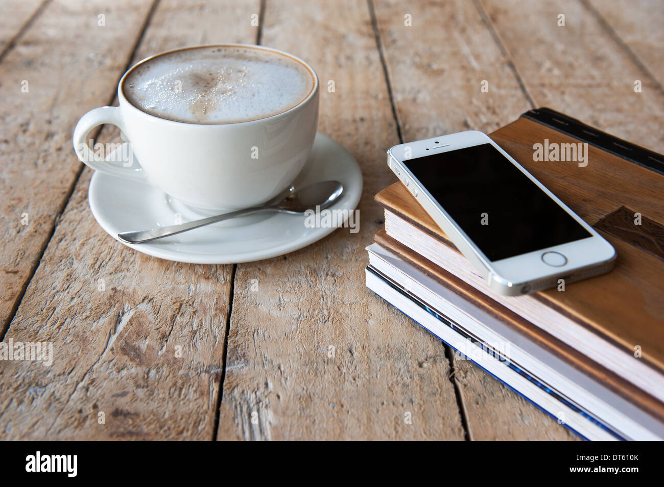 IPhone 5 s auf Bücherstapel neben einer Tasse schaumiger Kaffee. Stockfoto