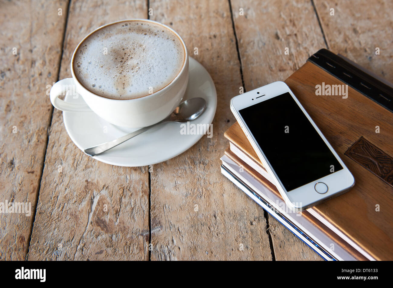 IPhone 5 s auf Bücherstapel neben einer Tasse schaumiger Kaffee. Stockfoto