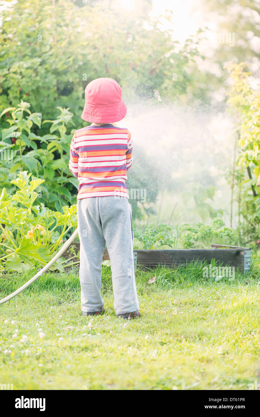 Lifestyle Sommer-Szene. Kleine Mädchen Bewässerung Garten Pflanzen und Gemüse mit Sprinkler. Stockfoto