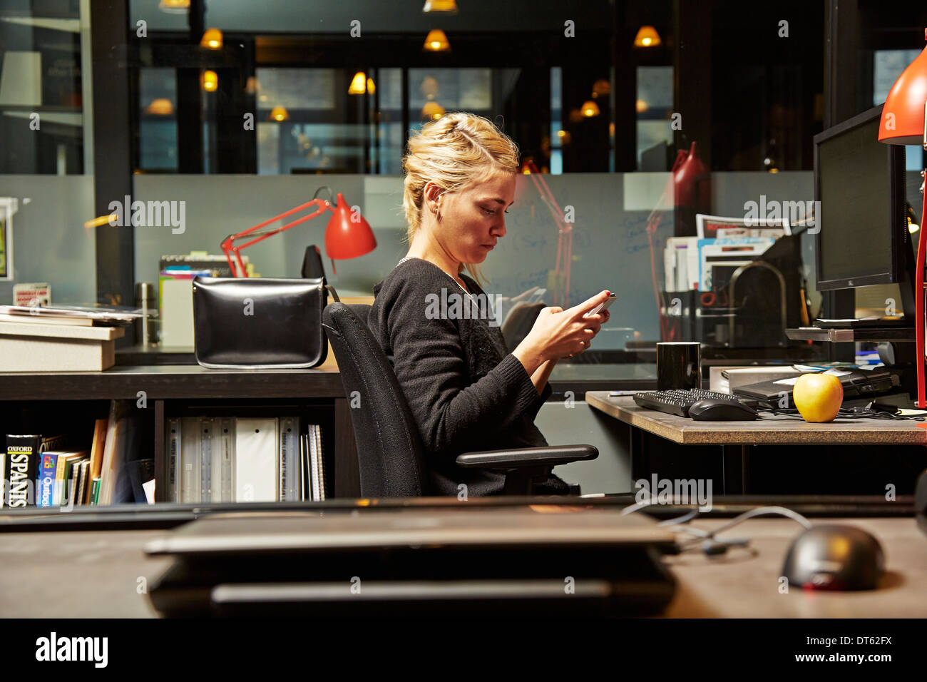 Weibliche Büroangestellte am Schreibtisch mit Handy Stockfoto