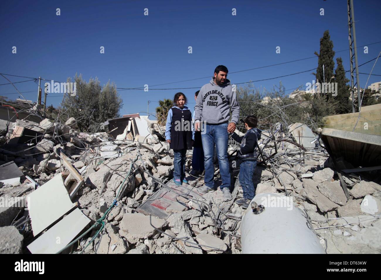 Jerusalem, Jerusalem, Palästina. 10. Februar 2014. Ein palästinensischer Mann steht mit seinen Kindern auf den Trümmern seines Hauses, nachdem es durch israelische Gemeinde Bagger abgerissen wurde, die die Behörden ohne städtische Berechtigung in der Nachbarschaft "Wade Advent" von der Stadt von Silwan in Jerusalem am 10. Februar 2014 zu glauben. Israel räumt selten Genehmigungen der Palästinenser im Westjordanland, einschließlich Ost-Jerusalems zu bauen. Es hat mindestens 27.000 palästinensische Häuser und Strukturen abgerissen seit der Besetzung der West Bank in 1967, nach dem israelischen Komitee gegen Haus Abriss Stockfoto