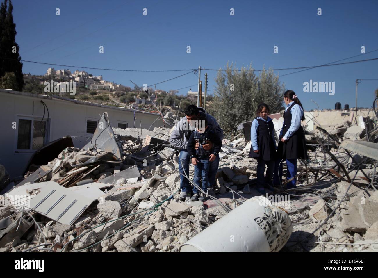 Jerusalem, Jerusalem, Palästina. 10. Februar 2014. Ein palästinensischer Mann steht mit seinen Kindern auf den Trümmern seines Hauses, nachdem es durch israelische Gemeinde Bagger abgerissen wurde, die die Behörden ohne städtische Berechtigung in der Nachbarschaft "Wade Advent" von der Stadt von Silwan in Jerusalem am 10. Februar 2014 zu glauben. Israel räumt selten Genehmigungen der Palästinenser im Westjordanland, einschließlich Ost-Jerusalems zu bauen. Es hat mindestens 27.000 palästinensische Häuser und Strukturen abgerissen seit der Besetzung der West Bank in 1967, nach dem israelischen Komitee gegen Haus Abriss Stockfoto