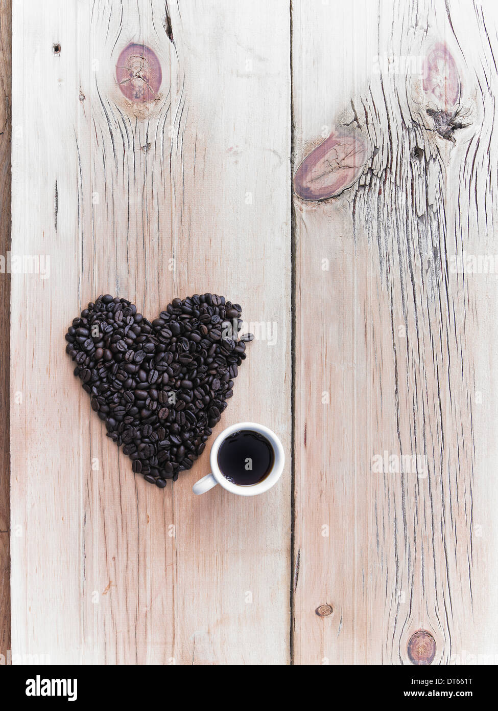 Draufsicht auf einen Haufen von Bio Kaffeebohnen in Form eines Herzens, angeordnet auf einer Tischplatte. Eine Tasse schwarzen Kaffee. Stockfoto