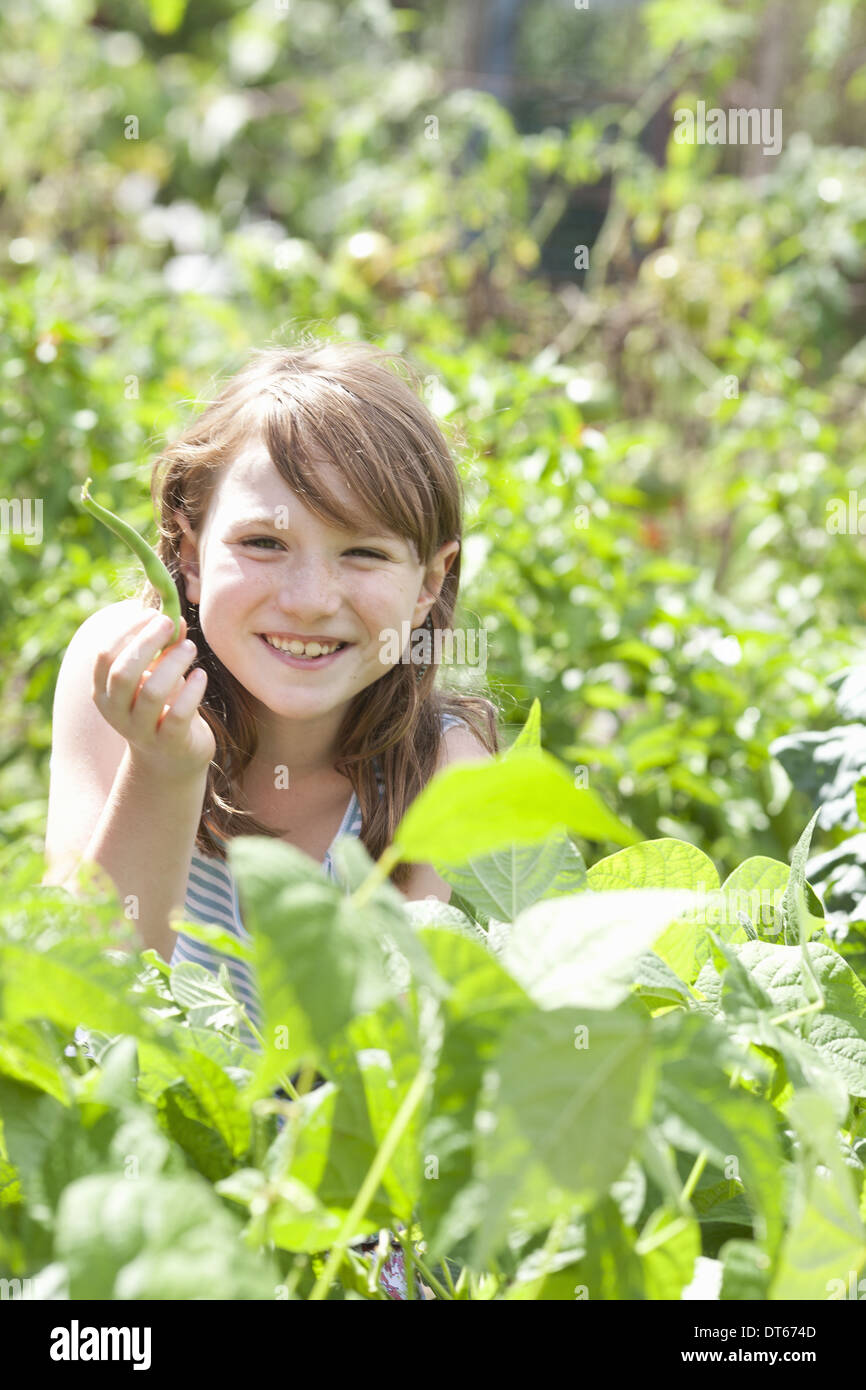Ein junges Mädchen sitzt unter dem frischen grünen Laub eines Gartens. Gemüse und Blumen. Pflücken frisches Gemüse. Stockfoto