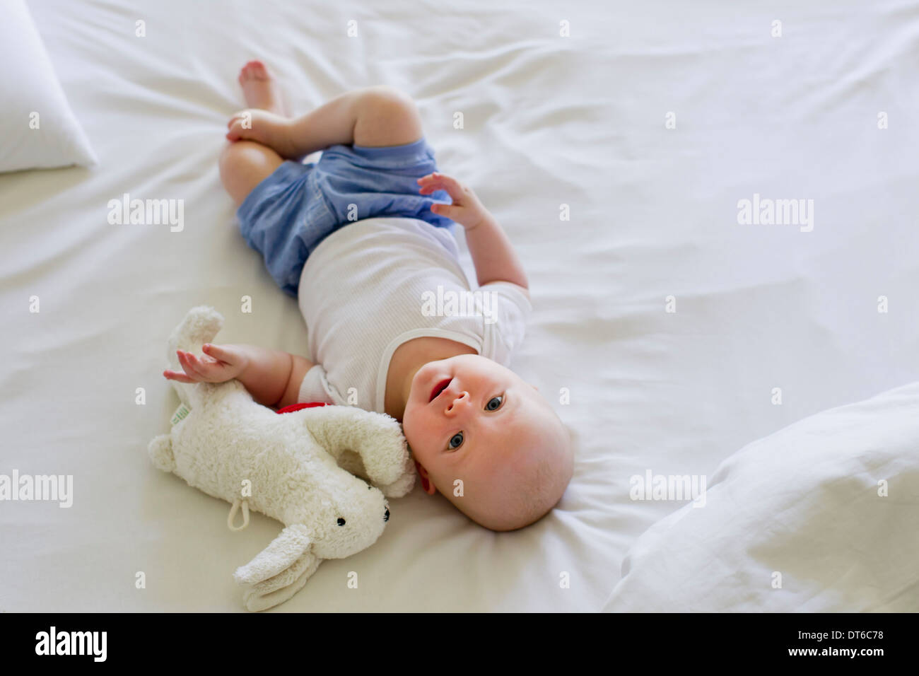 Babymädchen liegt auf Bettwäsche mit Stofftier Stockfoto