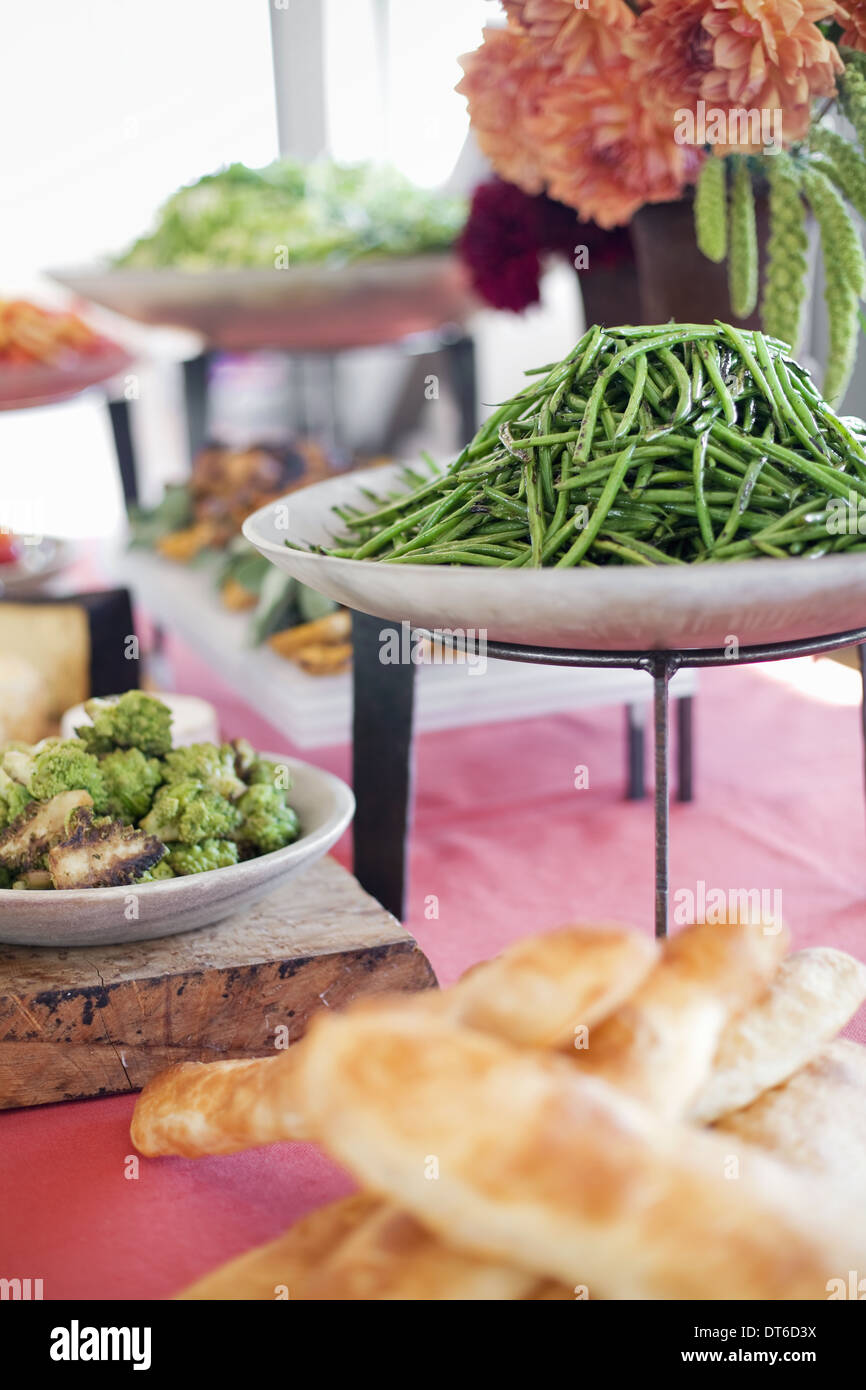 Salate, Gemüse und Obst auf dem Geschirr, ausgelegt für eine Party. Ein beladenen Tisch. Blumen in einer Vase.  Ein Bauernhof stand Garküche. Stockfoto