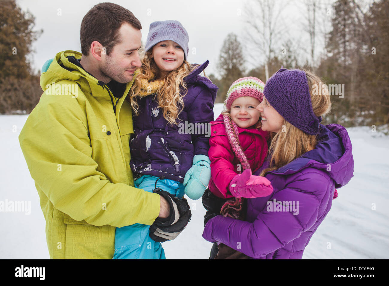 Mutter und Vater tragen Töchter im Schnee Stockfoto