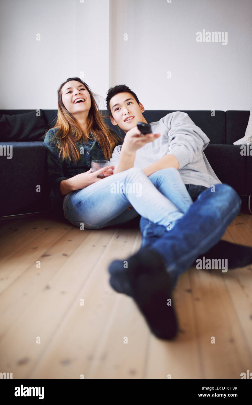 Hübscher junger Mann hält Fernbedienung Kanäle sitzen mit seiner schönen Freundin lachen während des Fernsehens. Stockfoto