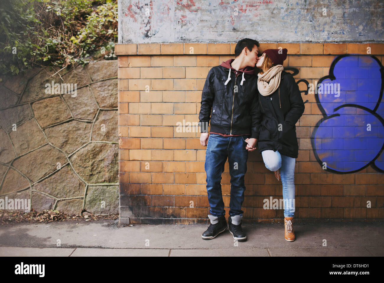 Liebevolle Teenager-Paar küssen im freien gegen eine Wand auf Straße. Mischlinge-paar in der Liebe. Stockfoto