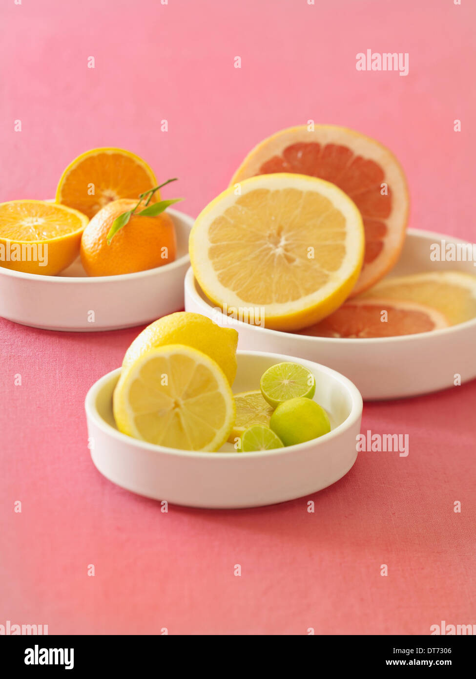 Eine weiße Platte mit Orangen, Blutorangen, Grapefruit, Zitronen und Limetten auf rosa Stoff Hintergrund. Stockfoto