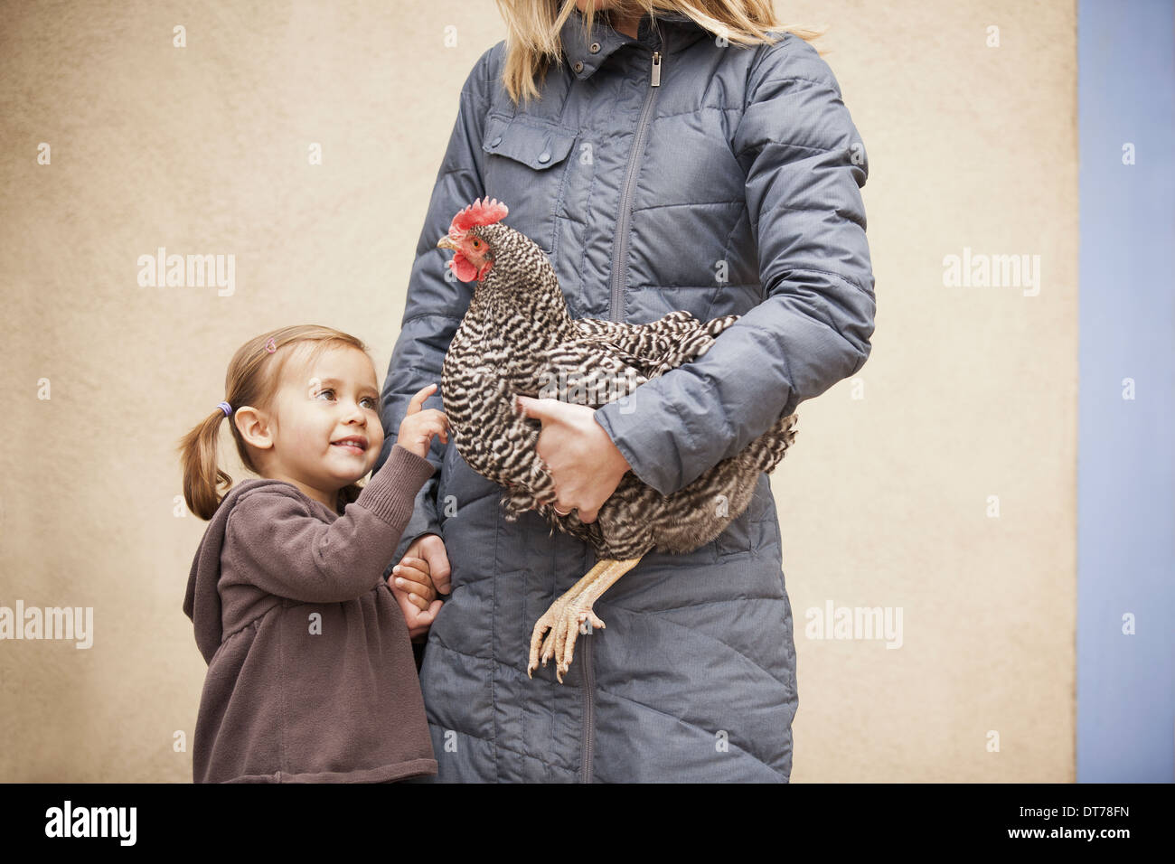 Eine Frau in einem grauen Mantel, Huhn mit einem roten Coxcomb unter einem Arm halten. Ein junges Mädchen neben ihr hielt ihre andere hand Stockfoto