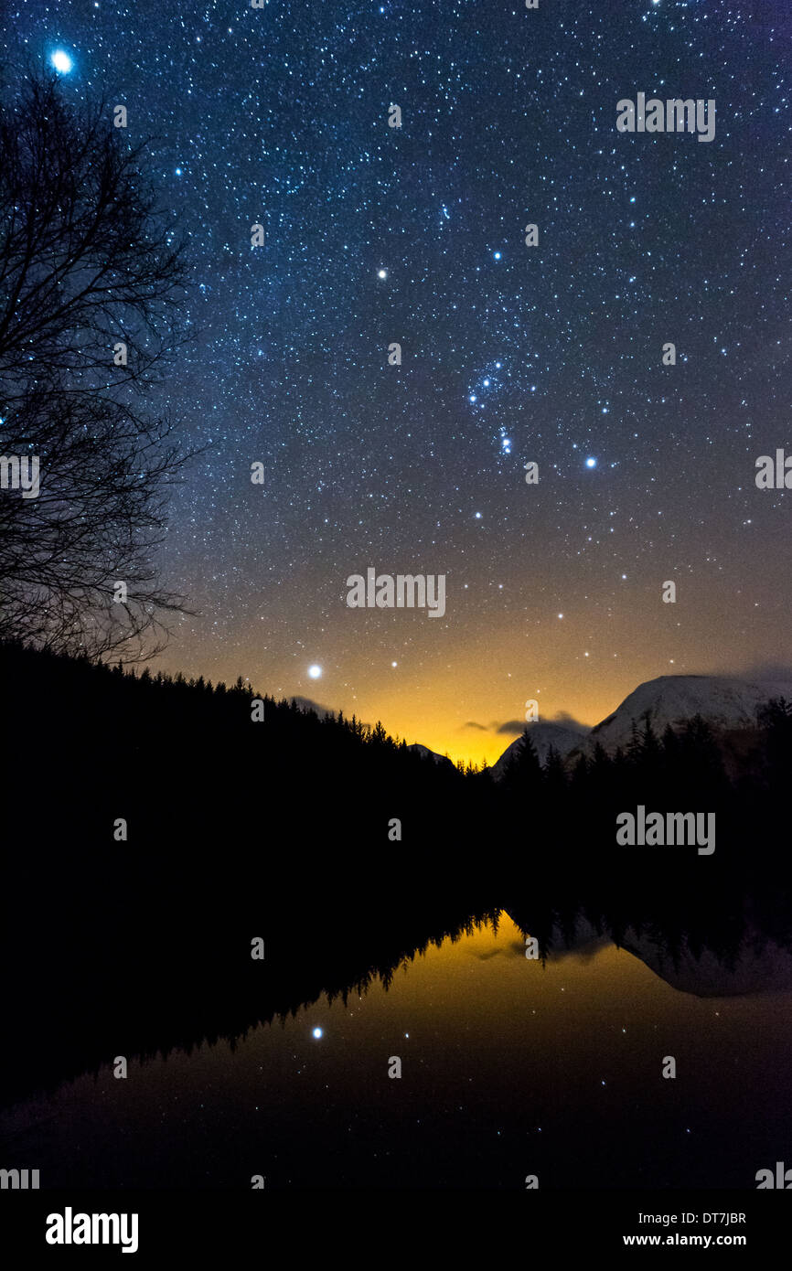 Astronomie-Foto zeigt das Sternbild des Orion & Orionnebel, Sirius, Jupiter spiegelt sich in Glencoe Lochan, Schottland, Vereinigtes Königreich Stockfoto