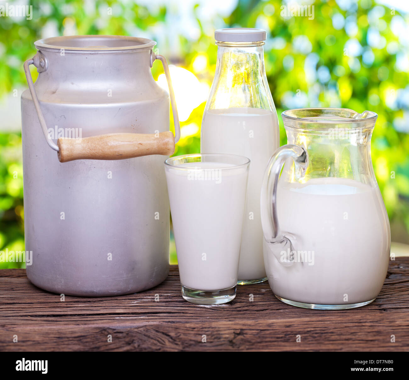 Milch in verschiedenen Gerichten auf dem alten Holztisch im Freien. Stockfoto