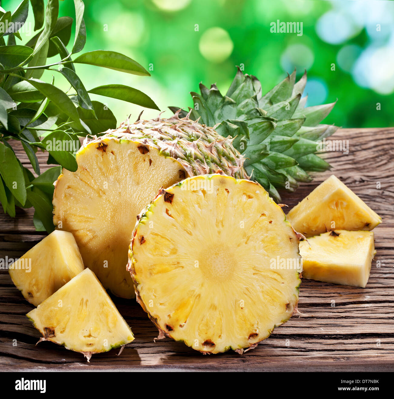 Ananas mit Scheiben auf einem Holztisch mit dunkelgrünem Laub auf dem Hintergrund. Stockfoto