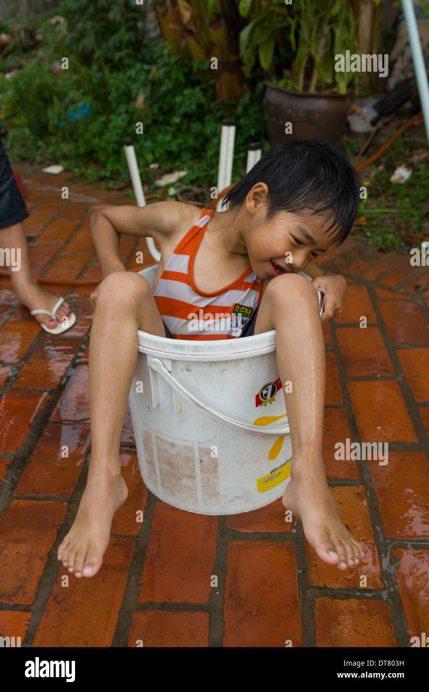 Young Lao Junge sitzt in einem Eimer mit Wasser, während Wasser kämpft auf Mue Nau, der mittlere Tag der Lao Neujahr (Pi Mai Lao), Luang Prabang, Laos Stockfoto