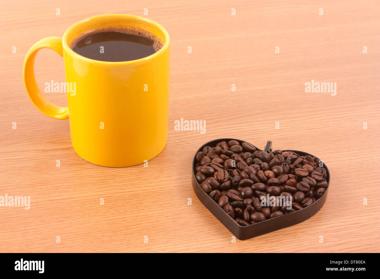 Tasse Kaffee mit Bohnen in Herzform auf Holz Hintergrund Stockfoto