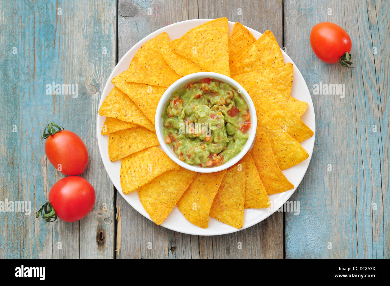 Mexikanische Guacamole Sauce mit Nachos und Tomate auf hölzernen Hintergrund Stockfoto