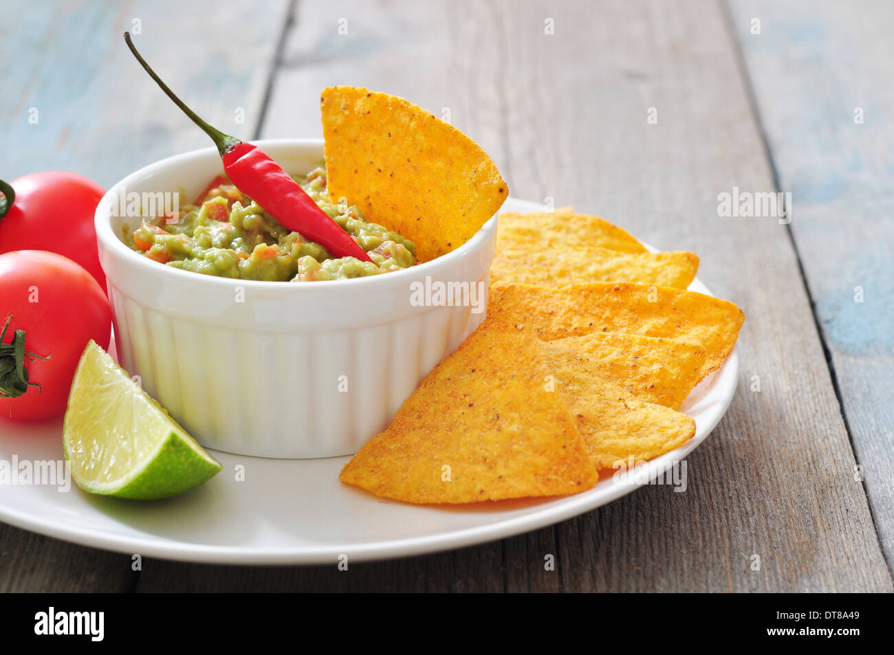 Mexikanische Guacamole Sauce mit Nachos und Tomate auf hölzernen Hintergrund Stockfoto