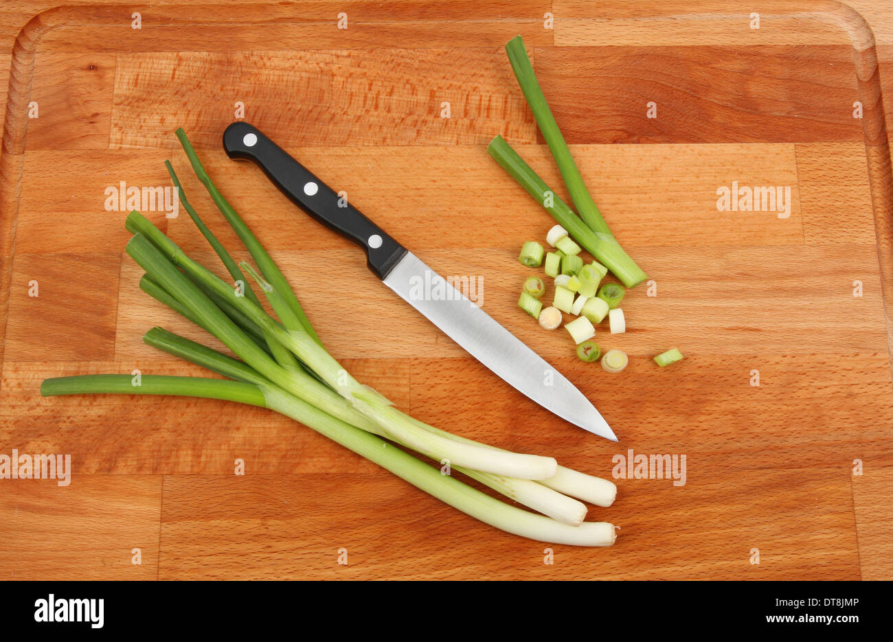 Salat Zwiebeln, ganze und schneiden mit einem Messer auf ein Schneidbrett aus Holz Stockfoto