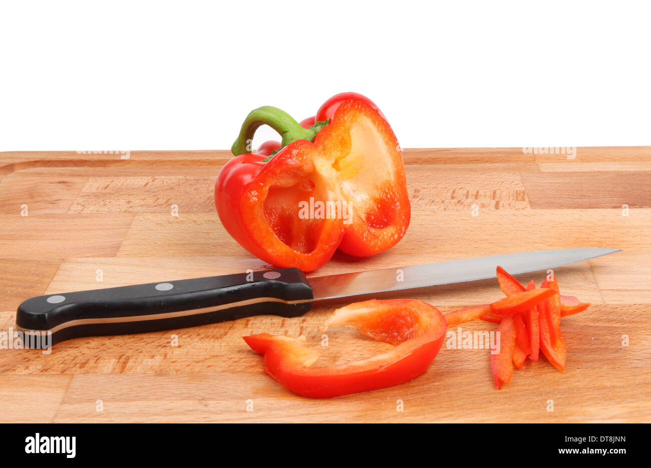 Schneiden Sie rote Paprika mit einem Messer auf einem Holzbrett vor einem weißen Hintergrund Stockfoto