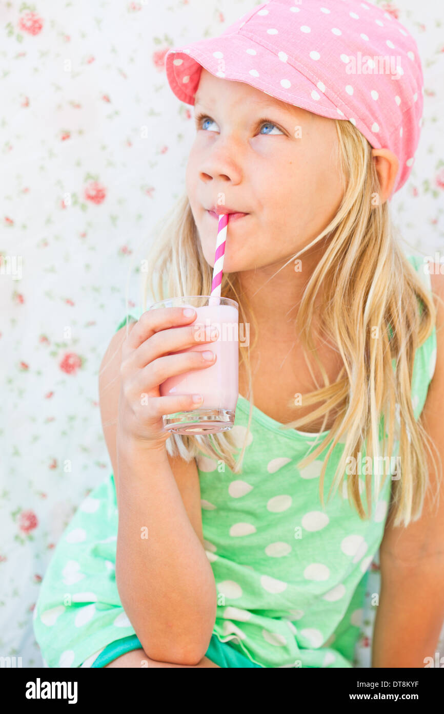 Süße junge Mädchen trinken Milch-Frucht-Smoothie mit gestreiften Stroh aus Glas in der hand gehalten Stockfoto