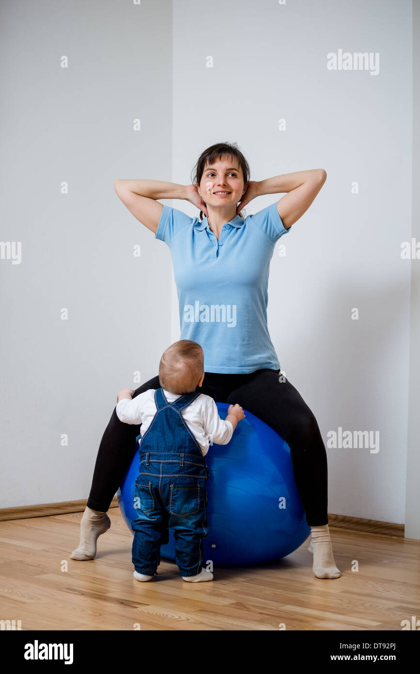Mutter Übungen auf großen blauen Fit-Ball zu Hause mit ihrem baby Stockfoto
