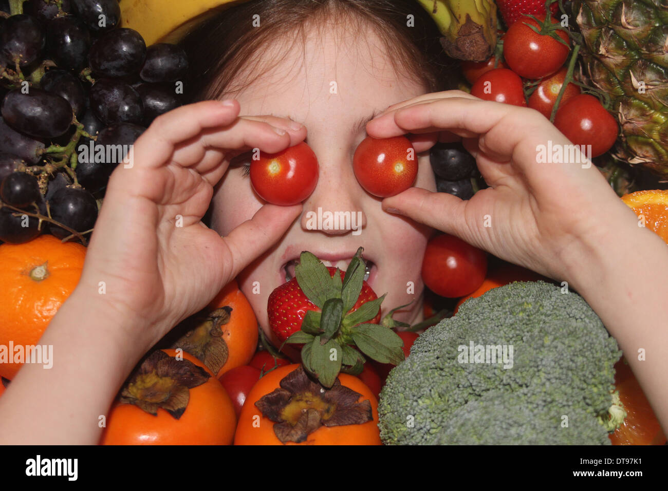 Kaukasische Mädchen Gesicht umgeben von Obst und Gemüse, fünf eine Tag, England, UK Stockfoto