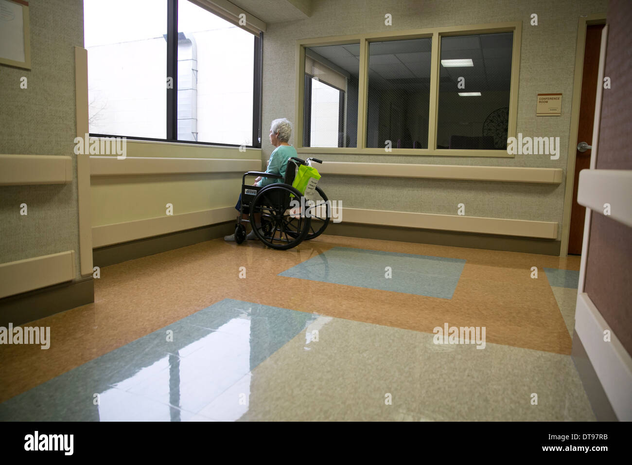 Hispanic Seniorin im Rollstuhl sitzt allein und schaut aus dem Fenster der Rehabilitationsklinik in Texas Stockfoto