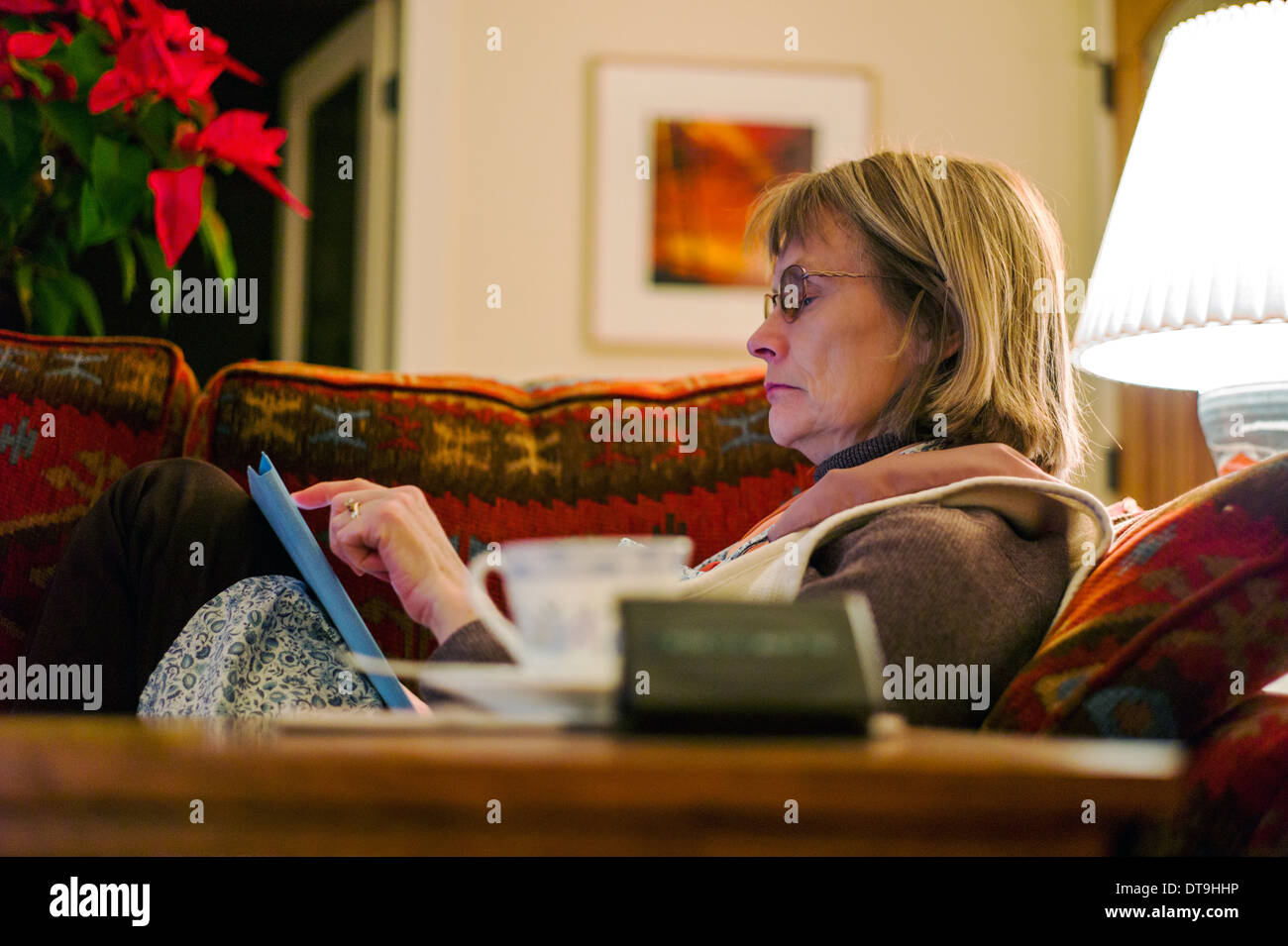 Mittlere gealterte Frau auf Sofa im Wohnzimmer auf einem Apple iPad arbeiten Stockfoto
