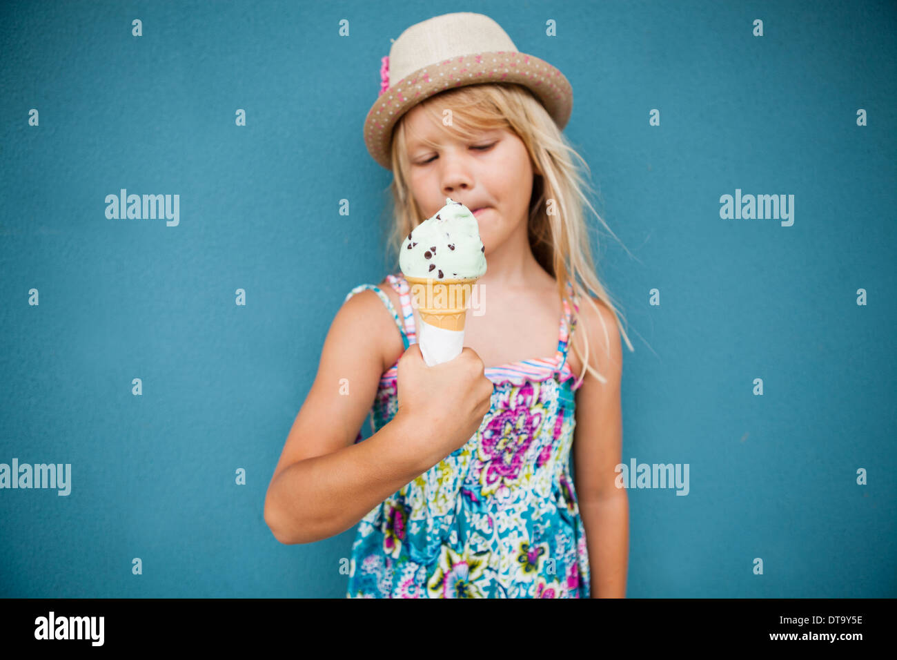Süße junge Mädchen mit Vanille Eis außerhalb gegen blaue Wand Hintergrund Stockfoto