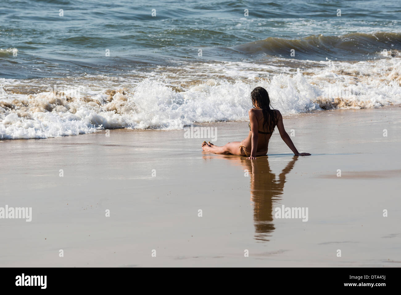 Eine junge Frau trägt Bikini sitzt im Sand von Anjuna Beach, Anjuna, Goa, Indien Stockfoto