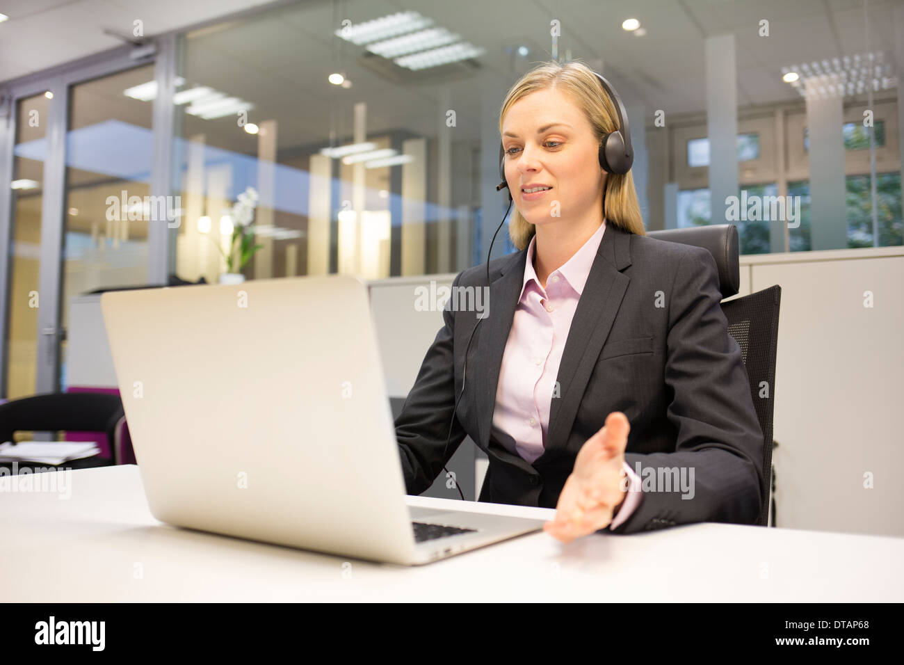 Hübsche Geschäftsfrau im Büro am Telefon mit Kopfhörer, video-Konferenz Stockfoto