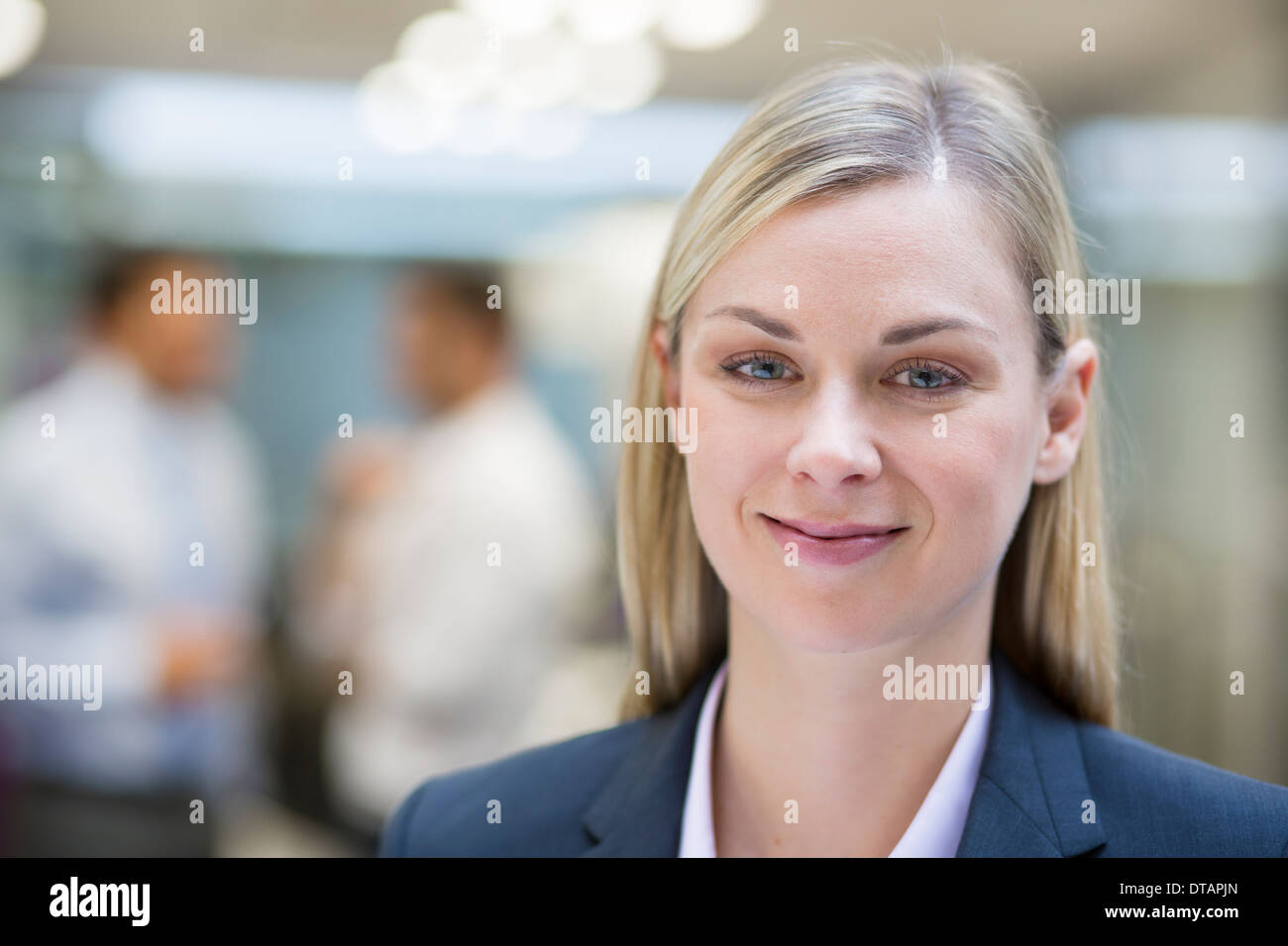 Blonde Unternehmerin während Kollegen miteinander reden, im Büro, auf der Suche Kamera posieren Stockfoto