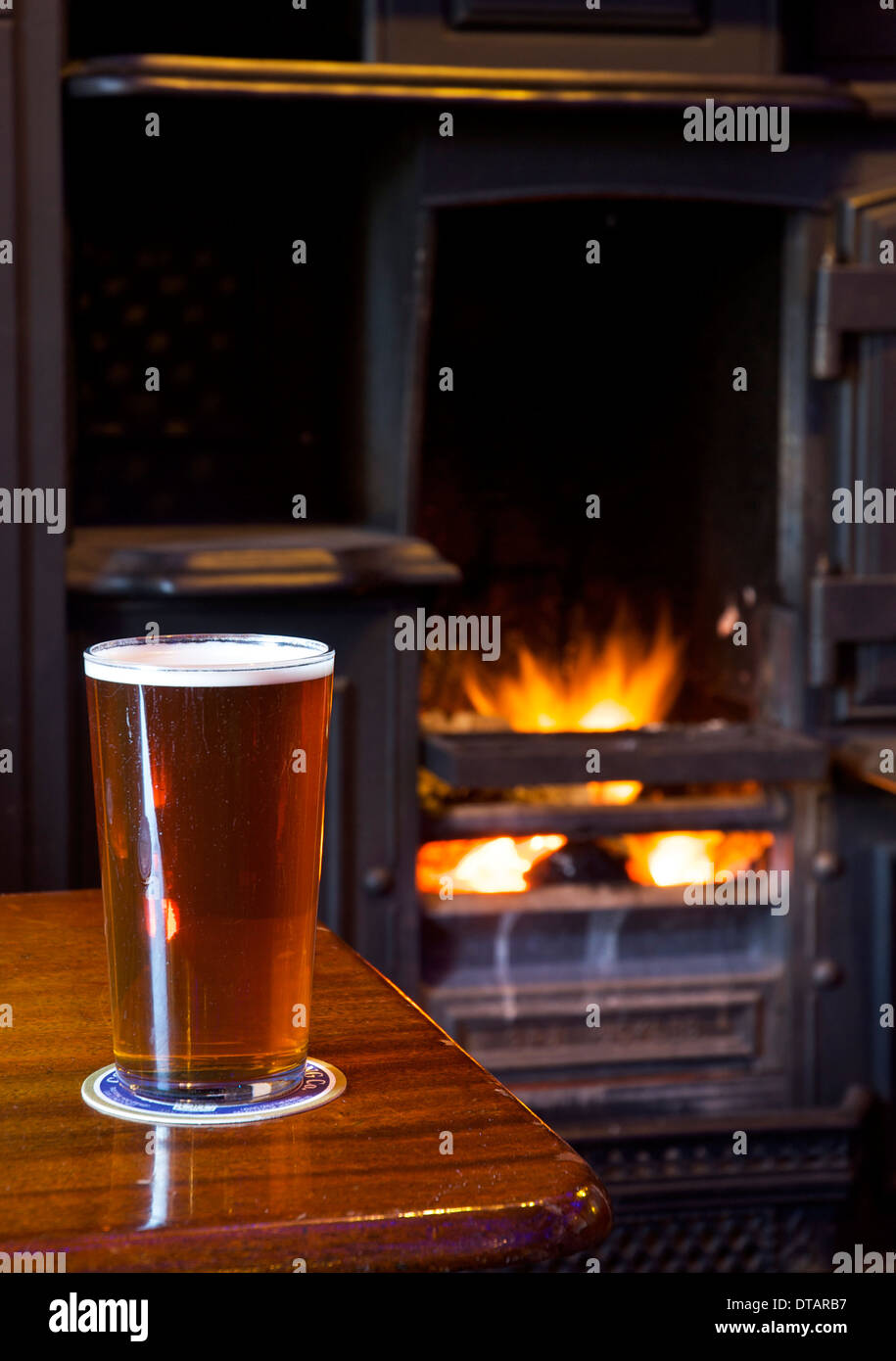 Ein Pint bitter auf einem Pub-Tisch mit offenem Feuer im Hintergrund Stockfoto