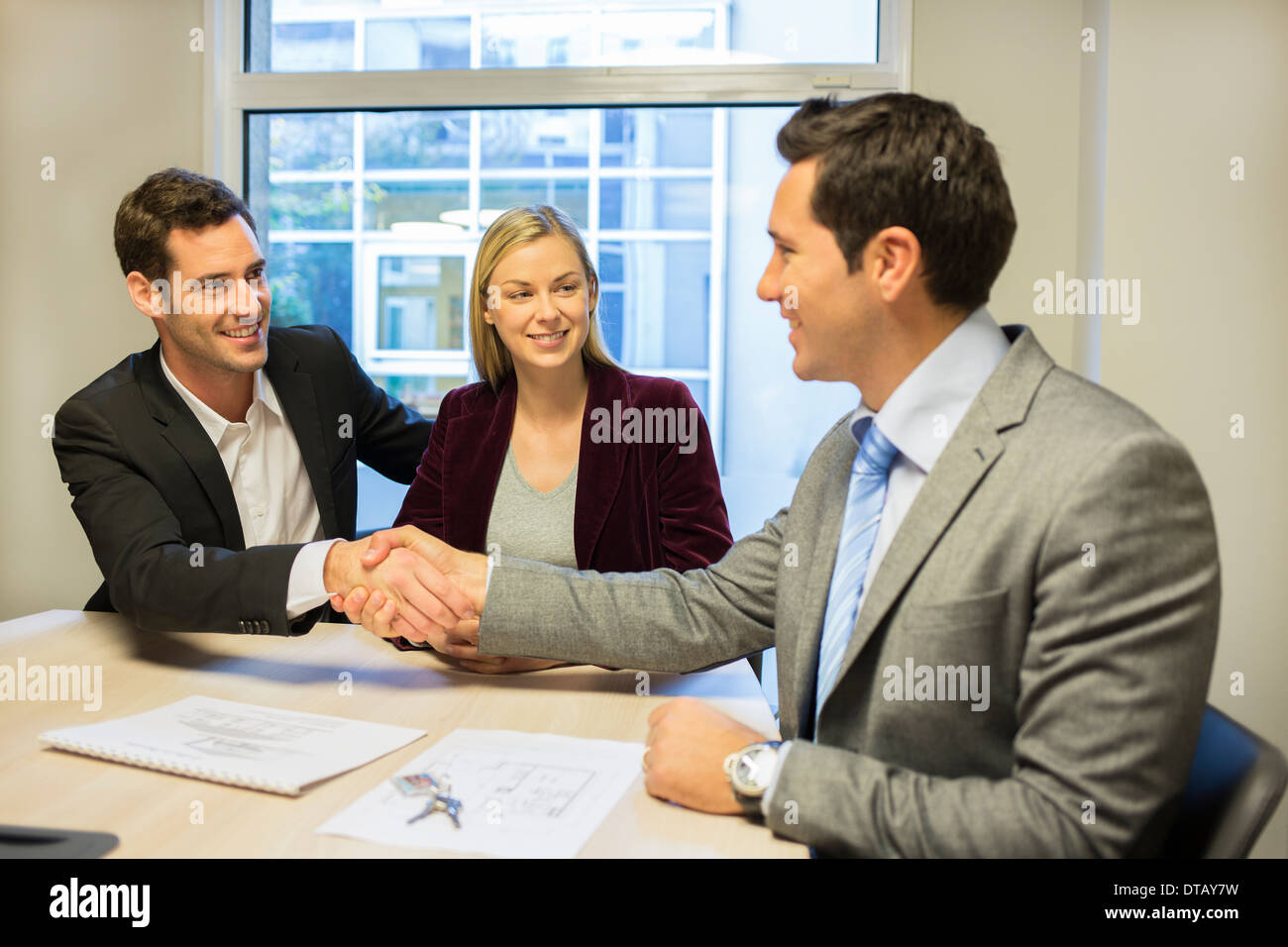 Paar im Tagungsraum mit finanzieller Berater, Vertrag, Händedruck, neue Eigentümer Stockfoto