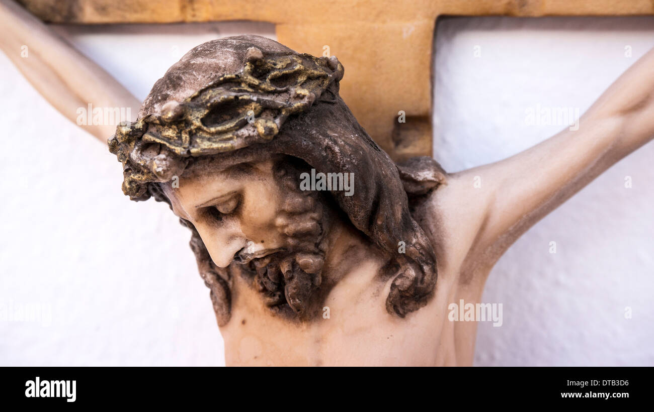 Detail Ansicht Kopf mit Dornenkrone auf billige bemaltem Gips Leiden Jesus am Kreuz auf weißem Putz Wand montiert Stockfoto