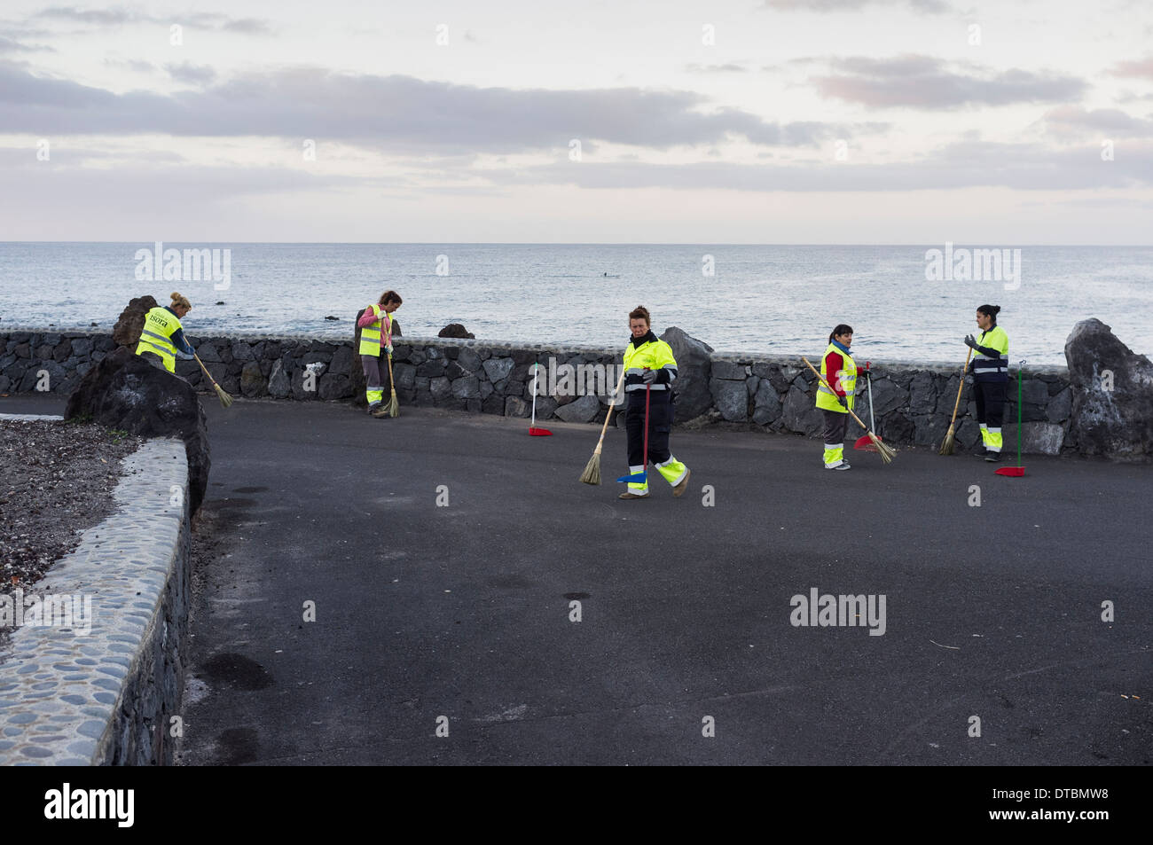 Arbeiterinnen des Rates reinigen und fegen über den Küstenweg in Playa San Juan, Teneriffa, Kanarische Inseln, Spanien. Stockfoto
