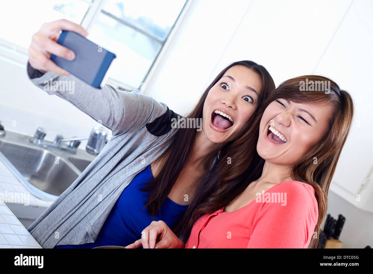 Zwei junge Frauen in Küche nehmen Selbstbildnis mit Handy Stockfoto
