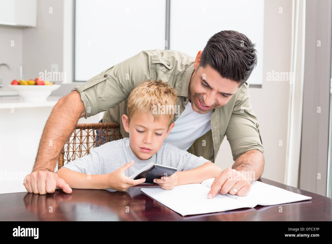 Lächelnd Vater Sohn mit Mathe-Hausaufgaben am Tisch zu helfen Stockfoto