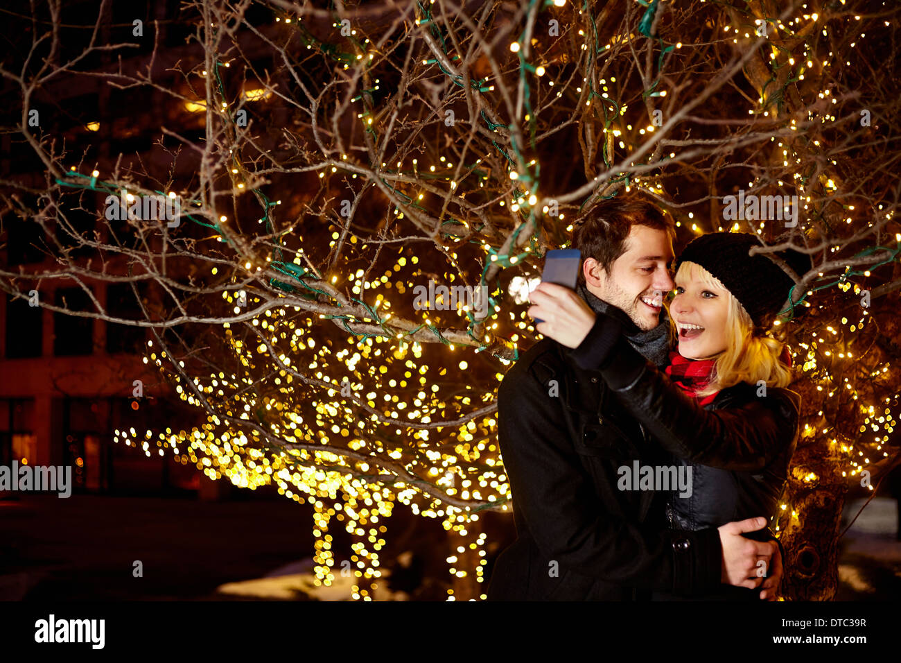 Junges Paar unter Selbstbildnis mit Stadt Weihnachtslichter Stockfoto