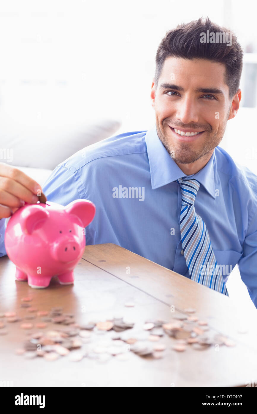 Gut aussehend Geschäftsmann, Münzen in die Piggy Bank Blick in die Kamera Stockfoto
