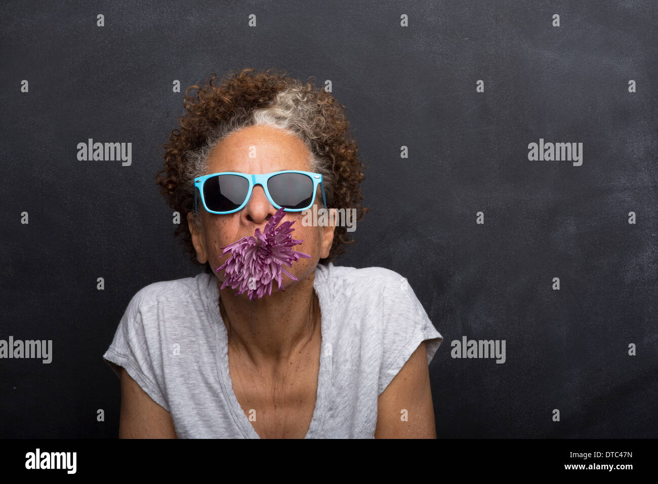 Studioportrait senior Frau mit Blume im Mund Stockfoto
