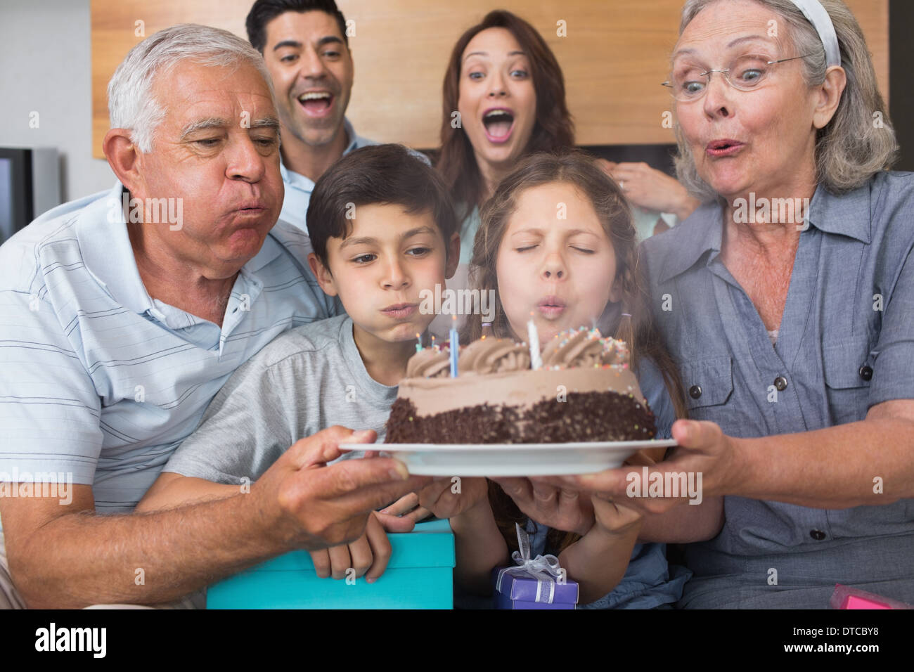 Großfamilie bläst Kerzen auf Kuchen im Wohnzimmer Stockfoto